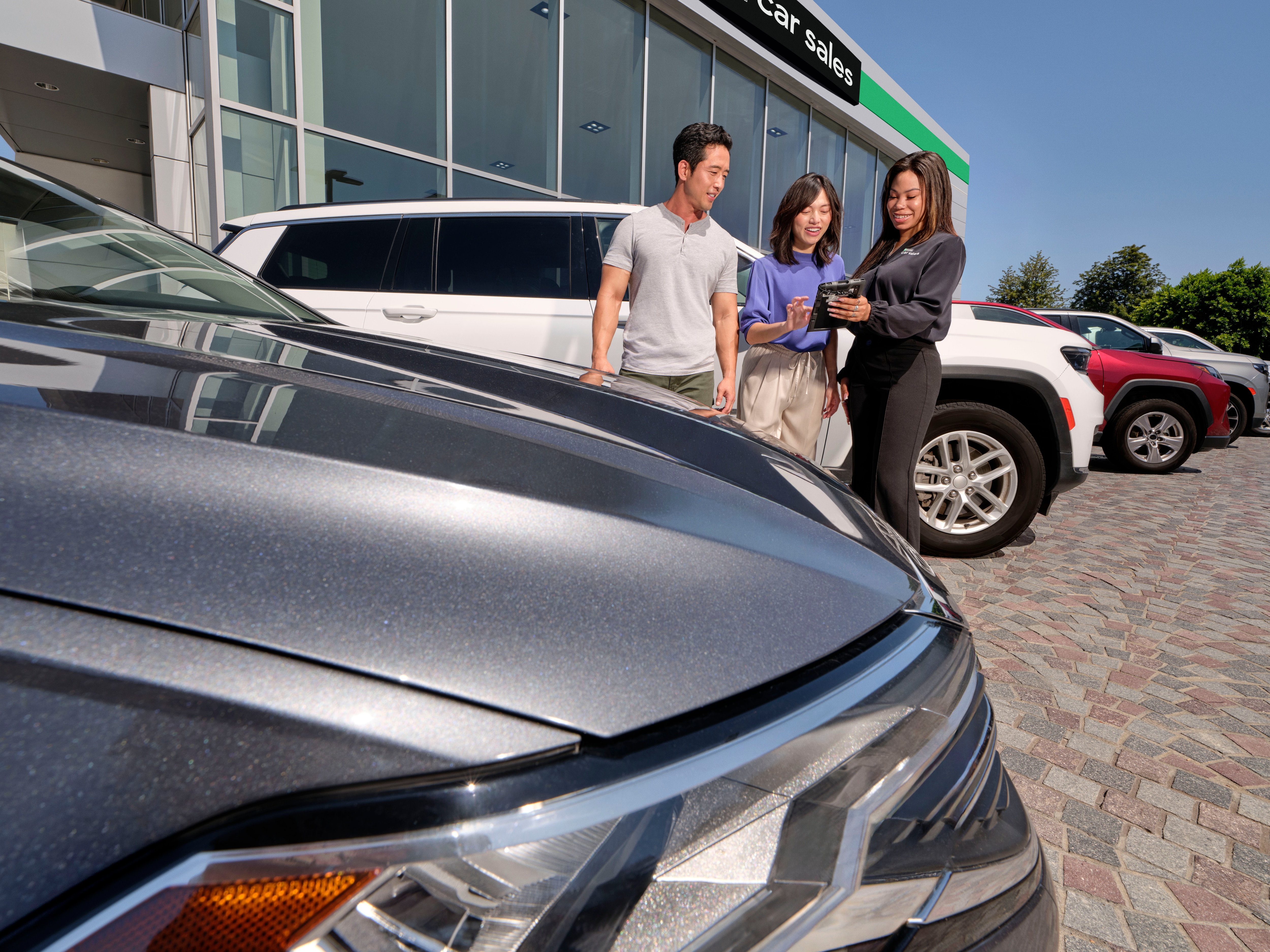 Man and woman talking to female car sales associate in the car lot